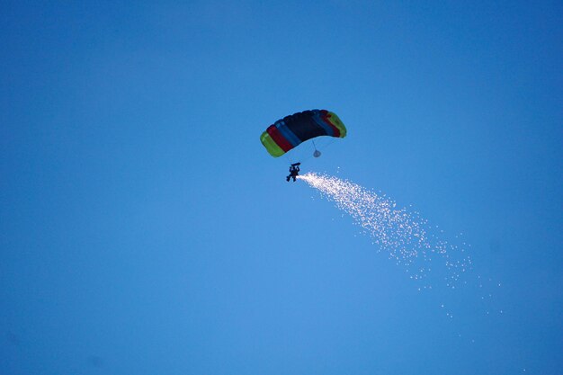 Zdjęcie niski kąt widoku ludzi latających na paragliderze na tle jasnego niebieskiego nieba