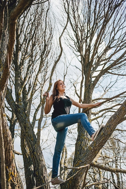 Zdjęcie niski kąt widoku młodej kobiety stojącej na gołym drzewie