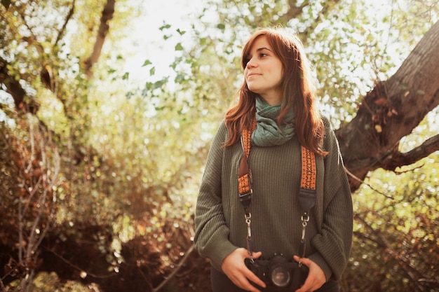 Zdjęcie niski kąt widoku młodej kobiety z kamerą stojącą w lesie