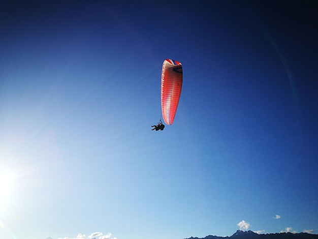 Zdjęcie niski kąt widoku osoby latającej na paragliderze na tle jasnego niebieskiego nieba