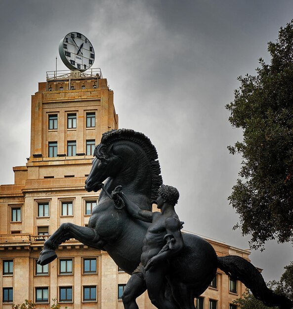 Zdjęcie niski kąt widoku posągu konia i człowieka przeciwko wieży zegarowej na placa de catalunya