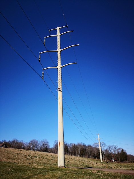 Zdjęcie niski kąt widoku słupa elektrycznego na polu na tle jasnego niebieskiego nieba