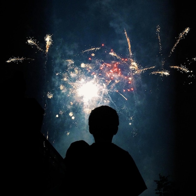 Zdjęcie niski kąt widoku sylwetki człowieka na tle fajerwerków na nocnym niebie