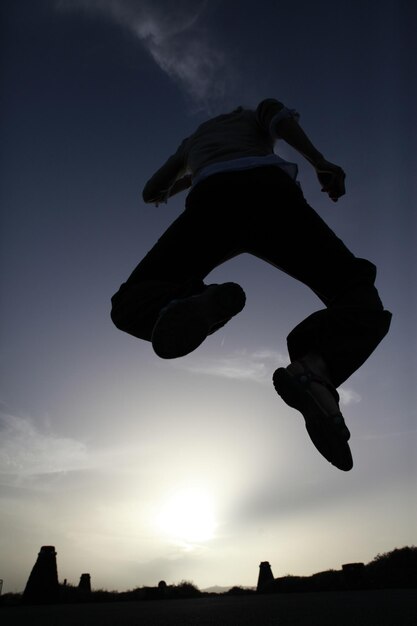 Zdjęcie niski kąt widoku sylwetki osoby skaczącej na polu na tle nieba
