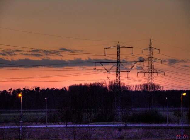 Niski kąt widoku sylwetkowych słupów elektrycznych na tle nieba w zmierzchu