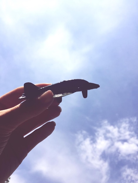 Zdjęcie niski kąt widoku z ręką trzymającą zabawkę samolotową na tle nieba