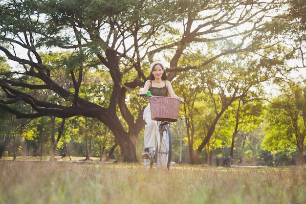 Niski kąt widzenia Azjatycka kobieta w zielonym stroju casual, siedząca z rowerem, patrząca na kamerę w publicznym parku z tłem przyrody