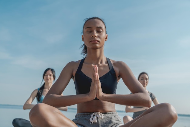 Niski kąt widzenia młodej kobiety na zajęciach jogi robi medytacji pozycji lotosu na plaży