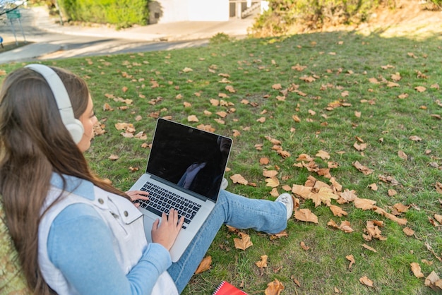 Zdjęcie niski kąt widzenia nastolatki korzystającej z komputera siedzącej na drzewie z jej zapasami obok niej