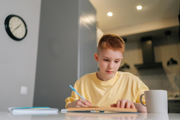 Niski kąt widzenia portret inteligentnego ucznia ucznia studiującego w domu, piszącego w zeszycie, odrabiającego lekcje, uczącego się, siedzącego przy stole