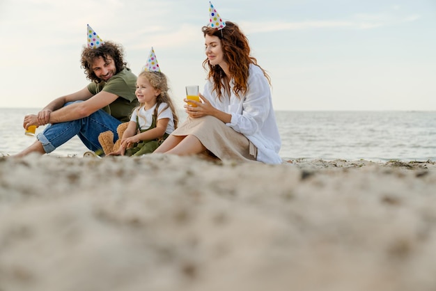 Niski Kąt Widzenia Rodziny W Imprezowych Czapkach Pijących Sok Pomarańczowy Na Plaży Rodzice I Córka