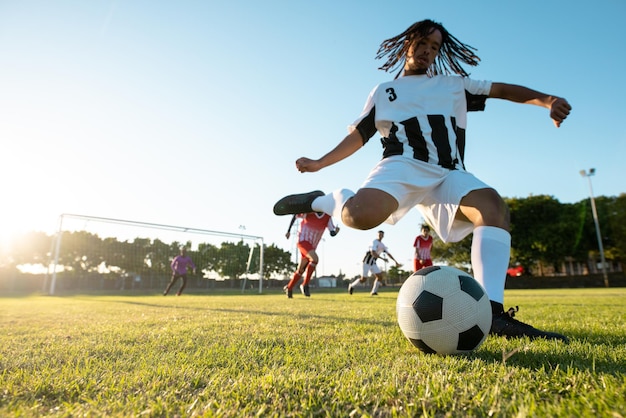 Niski kąt widzenia wielorasowego gracza kopiącego piłkę podczas meczu piłki nożnej przy czystym niebie