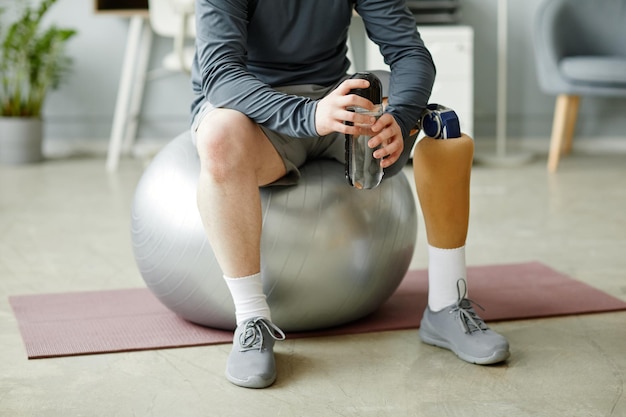 Niski Przekrój Zbliżenie Mężczyzny Z Protezą Nogi Siedzącej Na Piłce Fitness I Trzymającej Butelkę Z Wodą