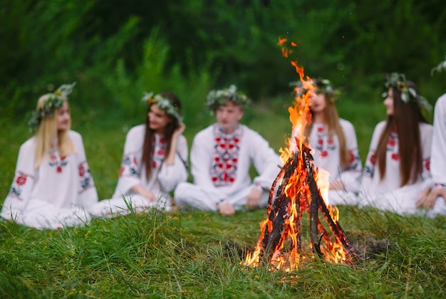 Zdjęcie noc przesilona, młodzi ludzie w słowiańskich ubraniach siedzący w lesie przy ogniu.