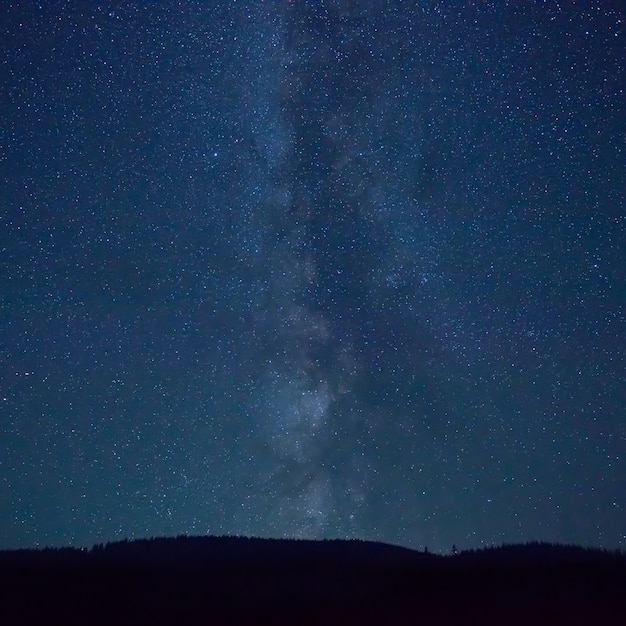 Nocne ciemnoniebieskie niebo z wieloma gwiazdami i galaktyką Drogi Mlecznej nad górą