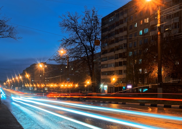 Nocne miasto z blaskiem, kałużami i niewyraźnymi liniami świateł