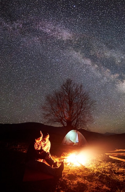 Nocny Kemping. Piesi Odpoczywający Przy Ognisku Pod Rozgwieżdżonym Niebem