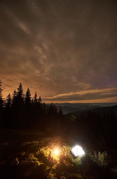 Nocny kemping z ludźmi przy ognisku pod nocnym rozgwieżdżonym niebem