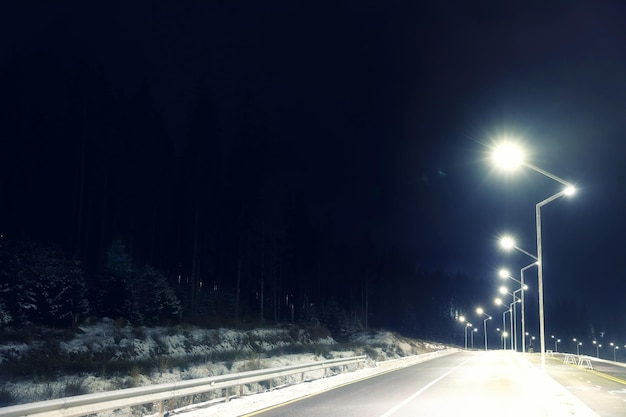 Nocny krajobraz z oświetloną drogą i lasem w zimie