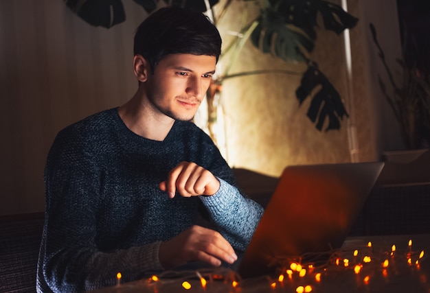 Nocny portret młodego biznesmena pracy w domu na laptopie. Girlandy