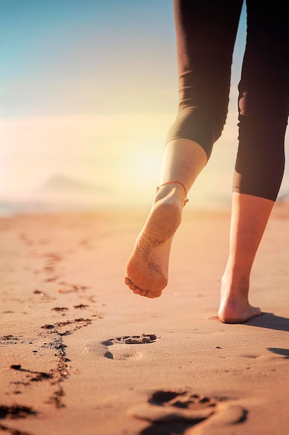 Nogi kobiety chodzącej po piasku plaży zostawiając jej ślady, gdy odchodzi