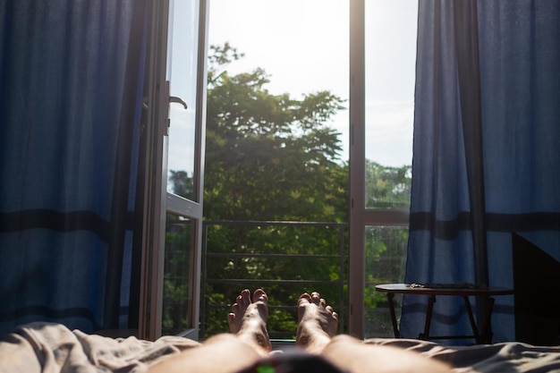 Nogi mężczyzny leżące na łóżku Widok na okno