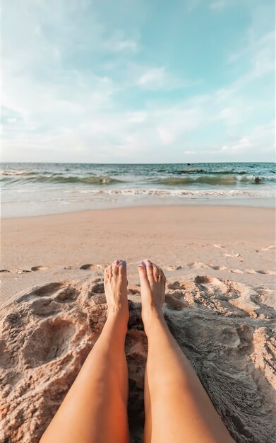 Nogi młodej kobiety leżące w piasku na plaży na tle oceanu i nieba