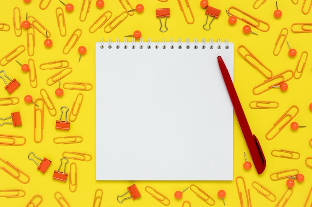 Zdjęcie notatnik i czerwony długopis na żółtym tle papieru. otwórz notatnik i zapasy na stole.