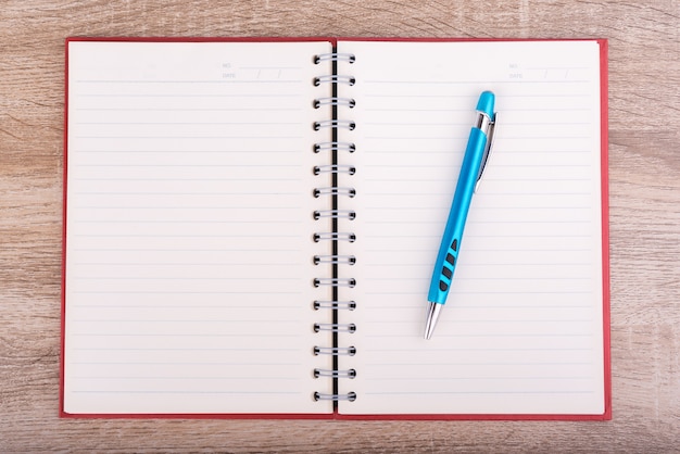 Notatnik lub pamiętnik i niebieski długopis na drewnianym stole.