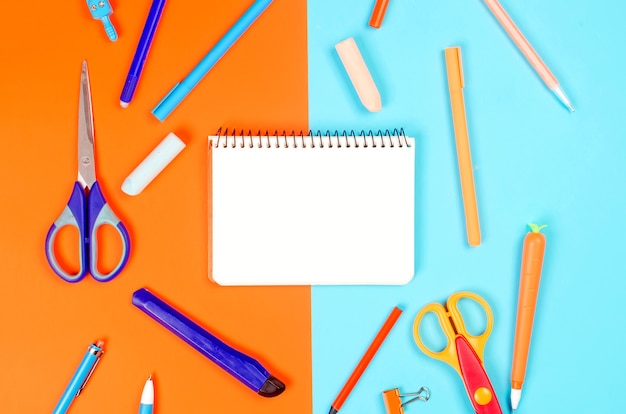 Notatnik, niebieski i pomarańczowy przybory szkolne na niebieskim tle