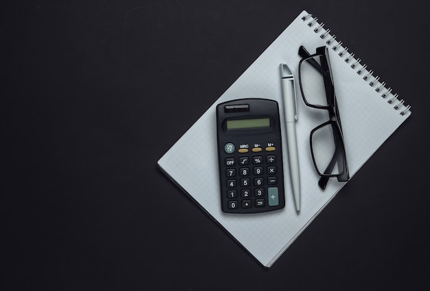 Zdjęcie notatnik z długopisem, kalkulatorem i okularami na czarno.