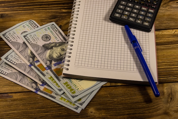 Notatnik z dolarami, długopisem i kalkulatorem na drewnianym biurku. Koncepcja finansowa