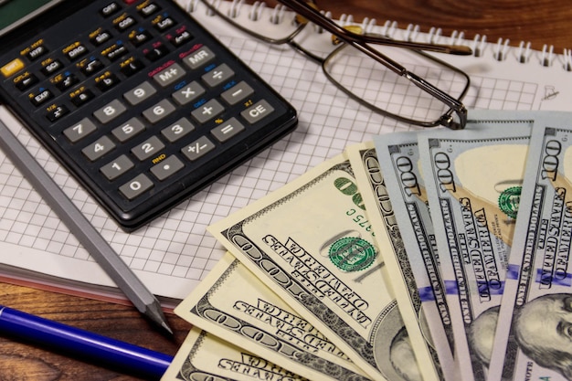 Notatnik z dolarami, długopisem, okularami i kalkulatorem na drewnianym biurku. Koncepcja finansowa. Rachunkowość biznesowa
