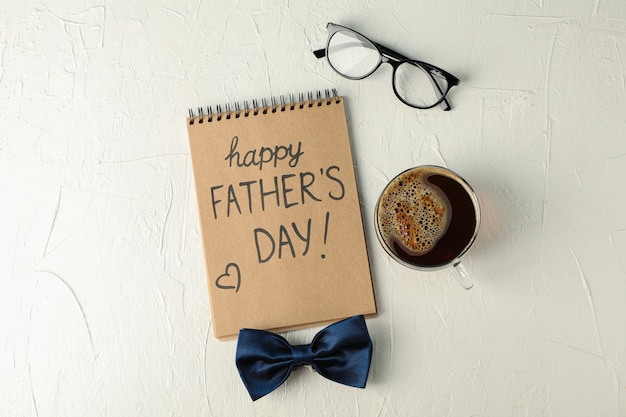 Notatnik z napisem szczęśliwy dzień ojców, niebieski muszka, filiżankę kawy i okulary na białym tle