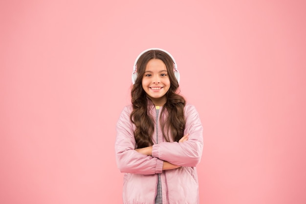 Nowa technologia dla dzieci Zabawa i rozrywka Nowoczesny styl życia Muzyka daje radość Szczęśliwe dziecko słucha muzyki różowe tło Mała dziewczynka nosi słuchawki odtwarzające muzykę