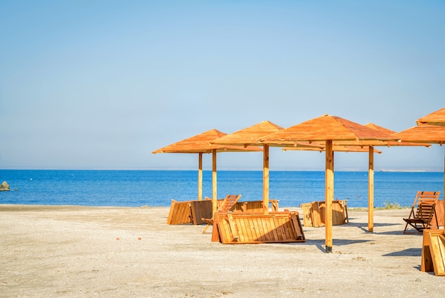 Nowe drewniane parasole, krzesło i leżaki na pustej plaży w słoneczny dzień