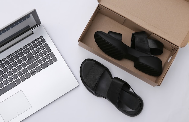 Nowe sandały w pudełku i laptop na białym tle. Widok z góry