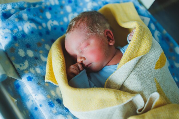 Nowo narodzone dziecko w niebieskim romperze Zdjęcie nowo narodzonego dziecka leżącego w kołysce Pierwsze zdjęcia dziecka