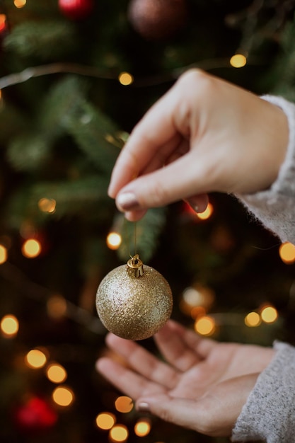 Nowoczesna brokatowa ozdoba w rękach na tle świątecznego drzewa w światłach Wesołych świąt Kobieta dekorująca choinkę błyszczącym złotym cacko zbliżenie Przygotowanie do świąt Bożego Narodzenia