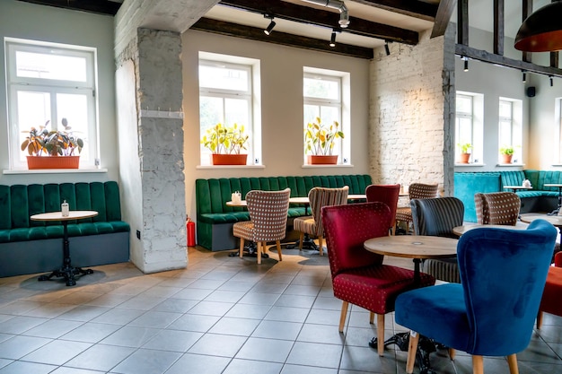 Nowoczesna przytulna restauracja z kolorowymi tapicerowanymi krzesłami i wygodnymi sofami Niezwykły projekt kawiarni z surowymi betonowymi ścianami i drewnianymi belkami dekoracyjnymi na suficie
