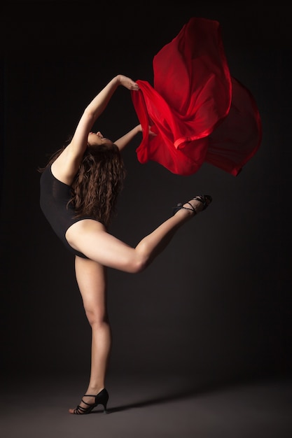 Nowoczesna tancerka z czerwonym materiałem pozuje na szaro