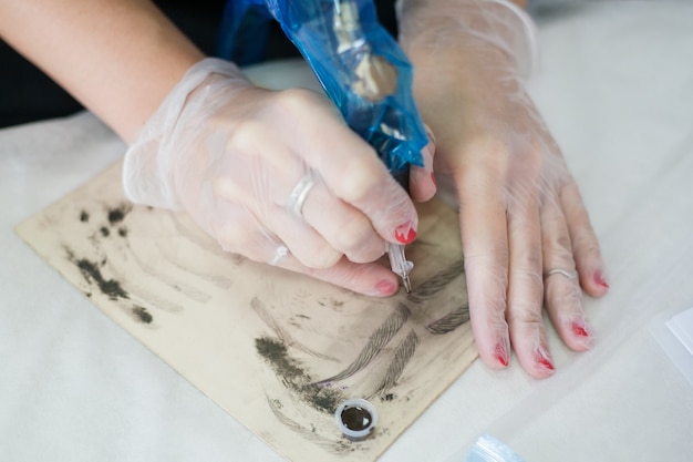Nowoczesna technika microbladingu. Zbliżenie dłoni kobiece kosmetyczka za pomocą maszynka do tatuażu do szkicowania brwi na papierze.