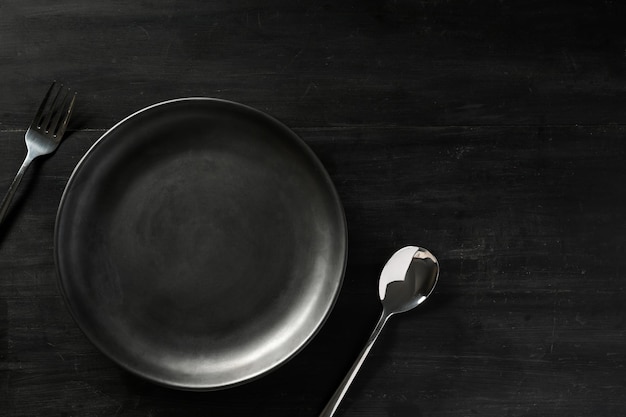 Nowoczesne czarne naczynia kuchenne pusta czarna płyta srebrna łyżka i widelec na drewnianym czarnym stole