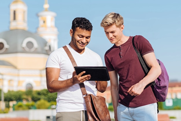 Nowoczesne technologie. Dwóch przyjaciół stojących obok siebie i uśmiechających się na twarzach, patrząc w dół