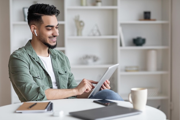 Nowoczesne technologie uśmiechający się młody arabski facet za pomocą cyfrowego tabletu w domu