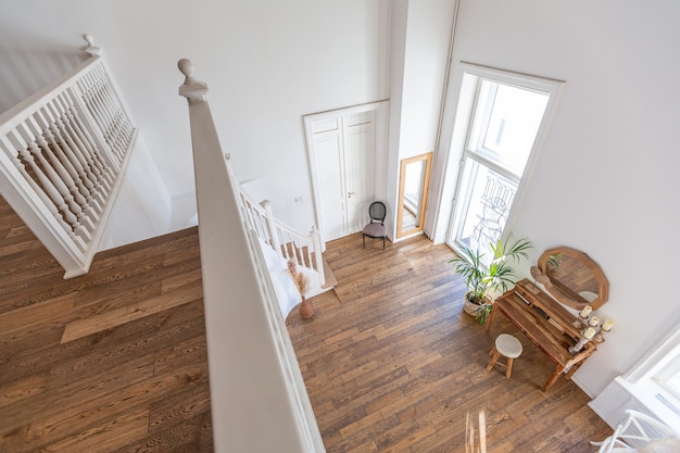 Nowoczesne wnętrze jasnego pokoju w dwupiętrowym mieszkaniu z elementami dekoracyjnymi w stylu balijskim z balkonem. białe ściany, drewniane podłogi i zabytkowe meble