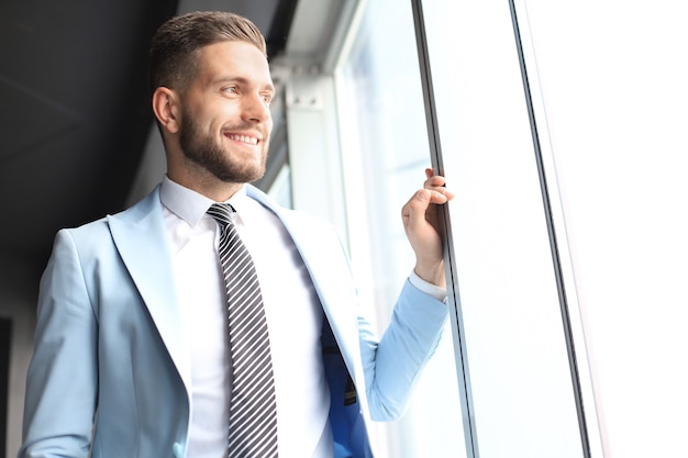 Zdjęcie nowoczesny biznes człowiek w formalwear stojący w pobliżu okna w biurze.
