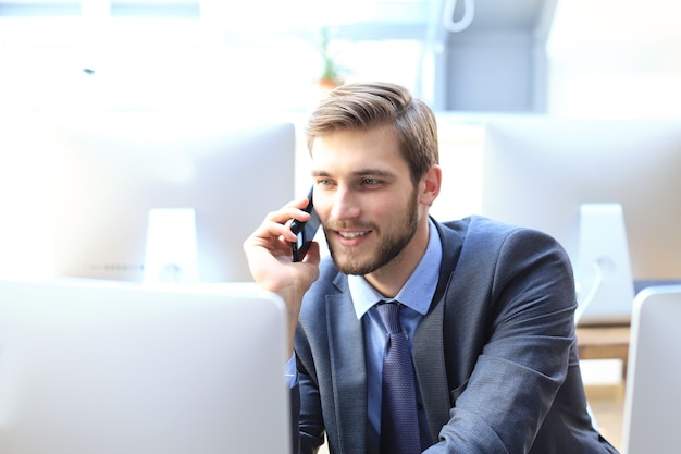 Nowoczesny biznesmen analizowania danych za pomocą komputera i rozmawia przez telefon siedząc w biurze.