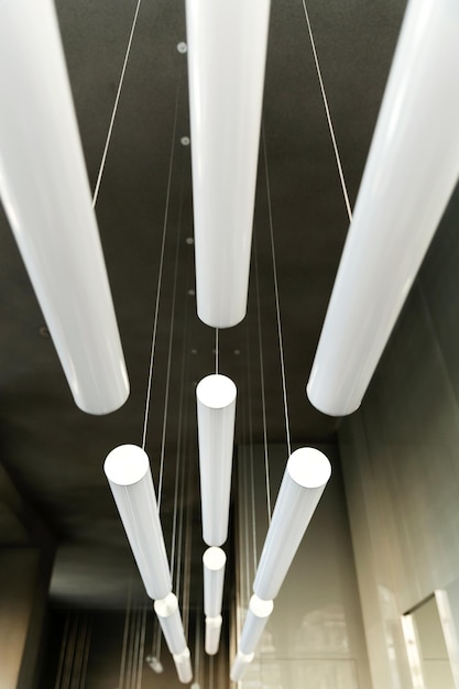 Nowoczesny design lamp we wnętrzu na podwieszanym suficie hali. Skład objętościowy długich cylindrycznych białych lamp fluorescencyjnych.