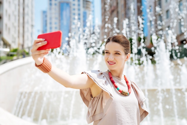 Nowoczesny Igen. Zadowolona ładna Kobieta Za Pomocą Aparatu W Smartfonie Podczas Robienia Selfie